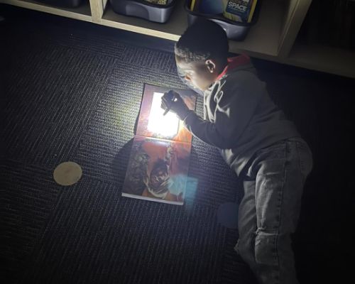  A student laying down reading a book in the dark with a flashlight.