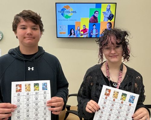 Two students hold up handouts with digital presentation behind 
