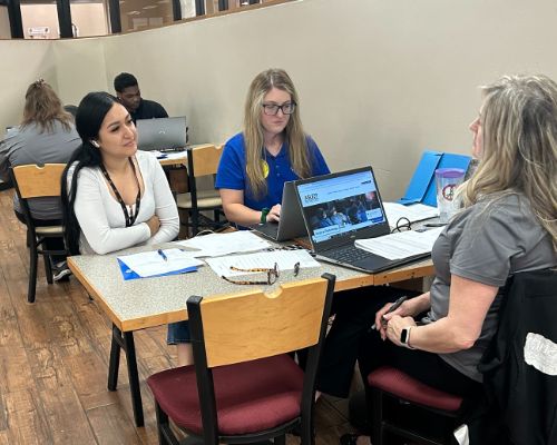  Student sits at library table with two advisers.