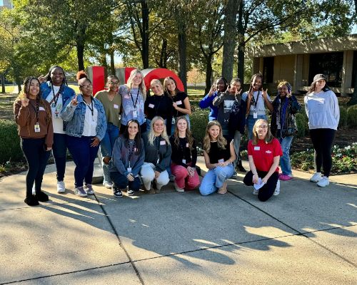  Group of students stand smiling outside the HOWL sign on the Astate campus