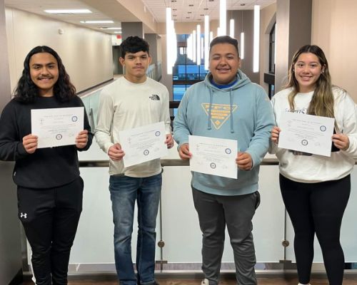  Four students hold certificates, smiling.